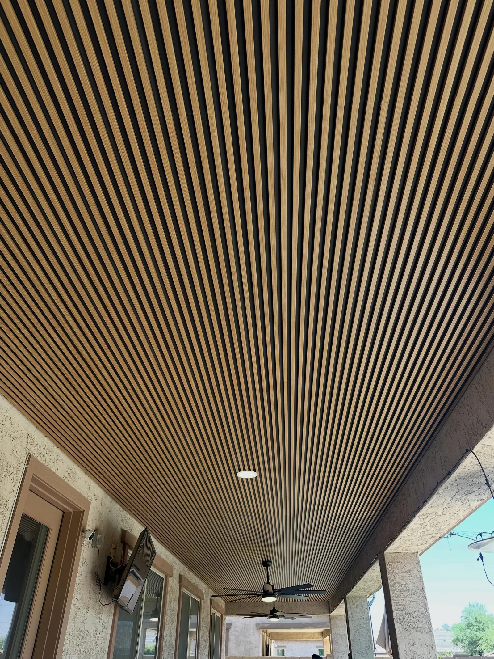 Linear wood slat ceiling over a covered patio with fans and recessed lighting