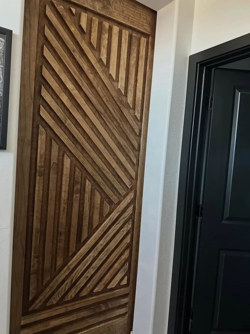 Diagonal slat door panel in warm stained wood beside a black casing