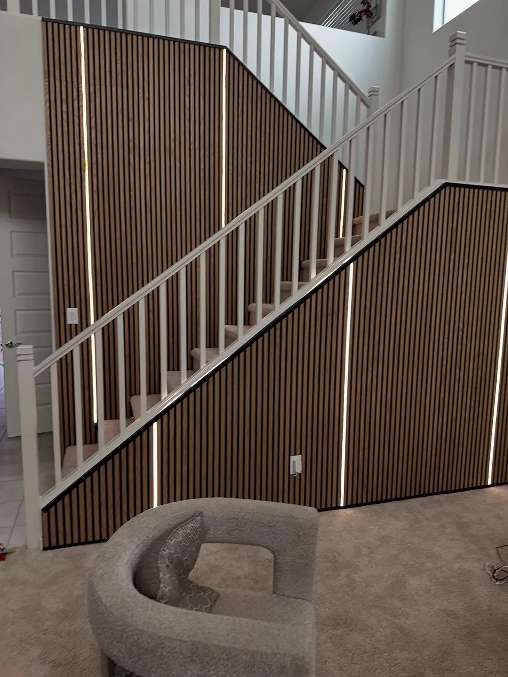 Two story wood slat accent wall along a staircase with thin LED strips between slats