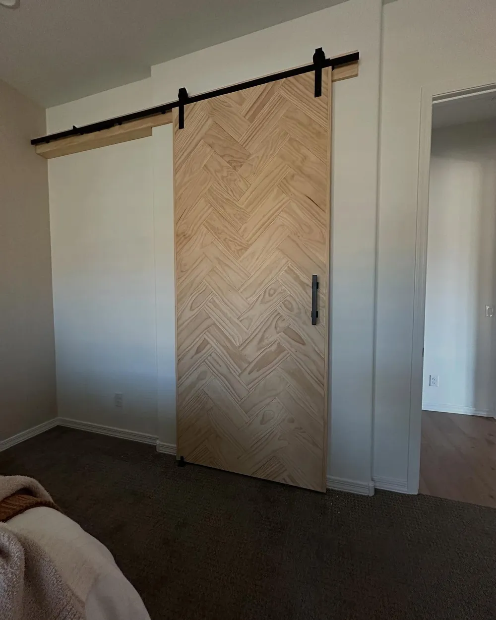 Herringbone patterned barn door in natural wood with matte black rail