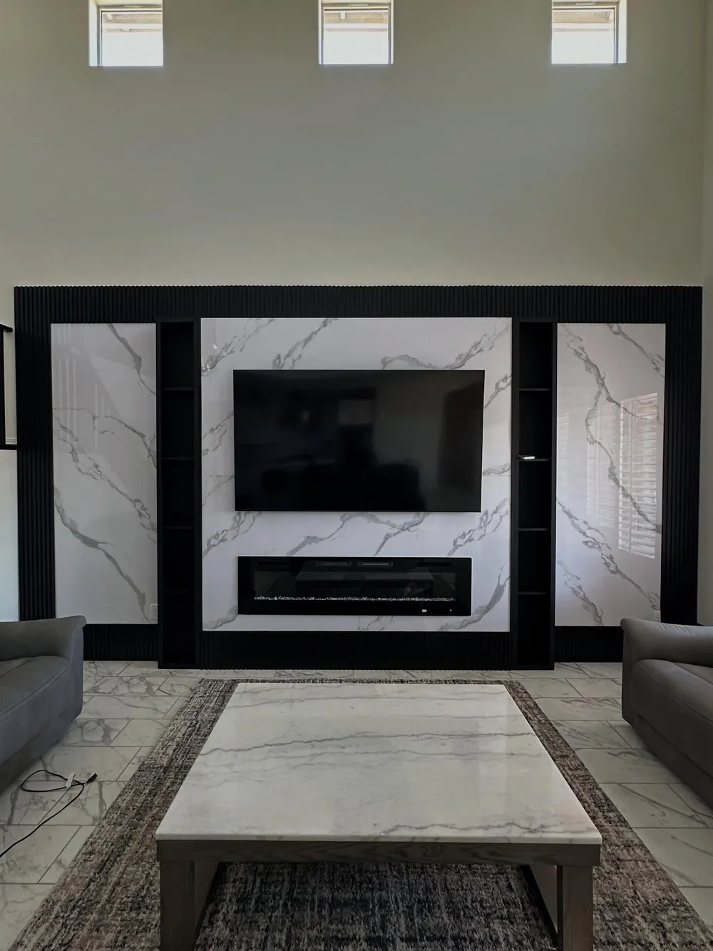 Fluted black trim and marble panels surround a fireplace wall beneath a vaulted ceiling.