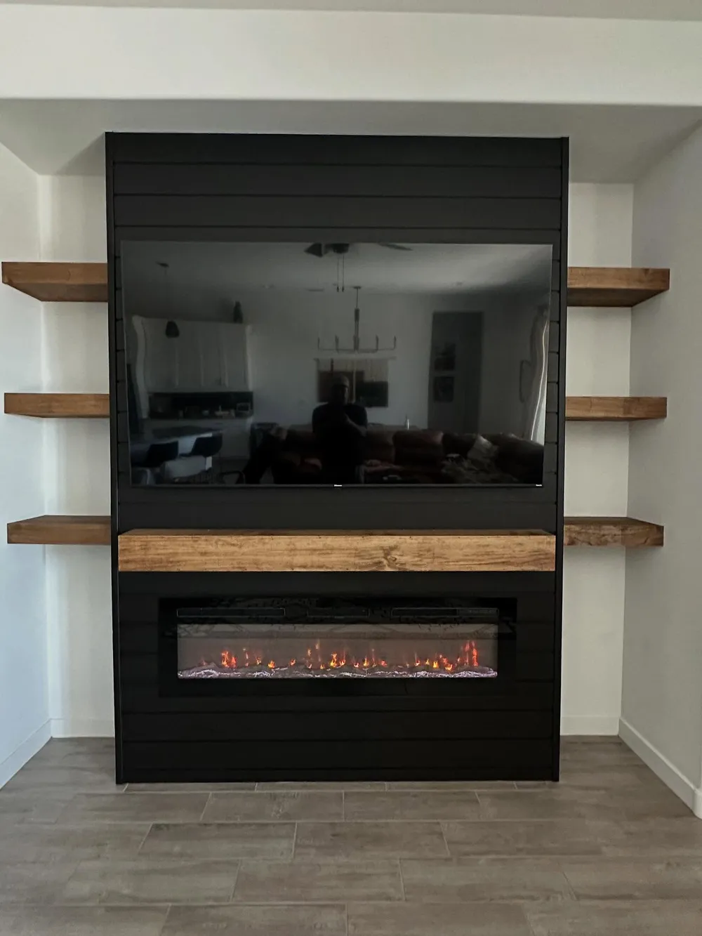 Black shiplap paneling meets walnut floating shelves and a matching mantel.