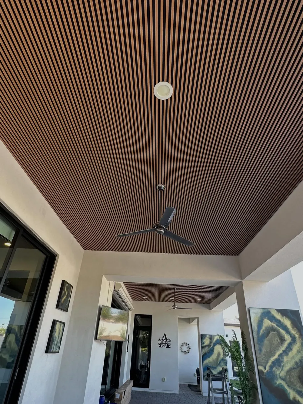 Warm wood slat ceiling spanning a covered patio with an outdoor fan