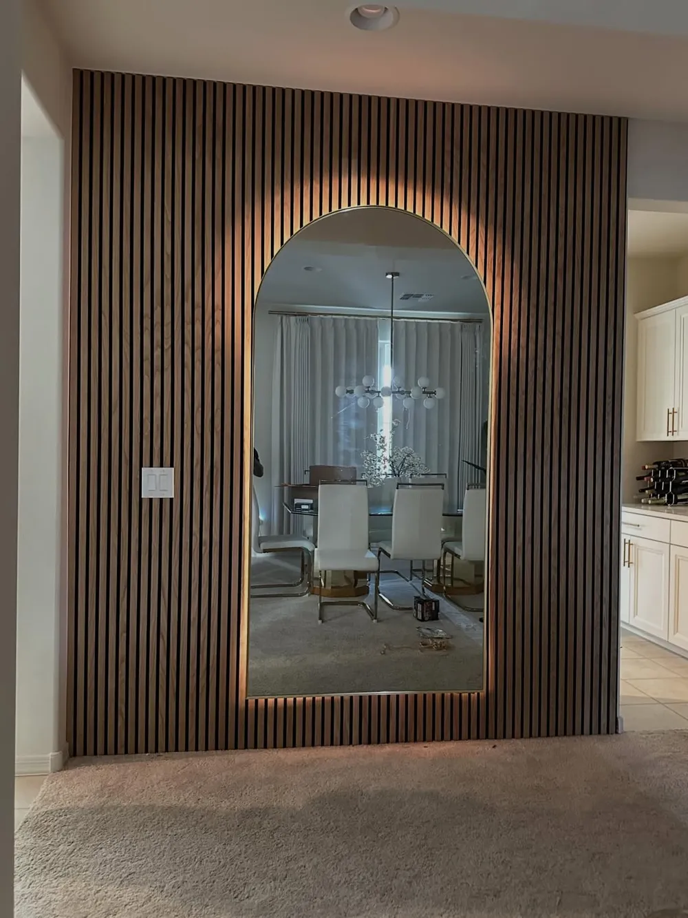 Arched mirror set into warm oak slat paneling with backlighting